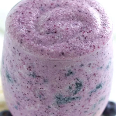 Healthy blueberry banana protein smoothie in a glass with fresh fruits around it