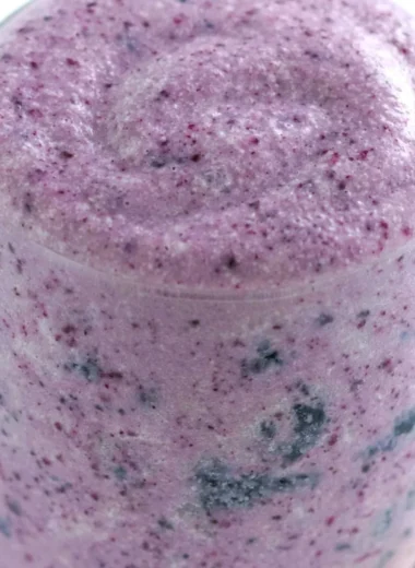 Healthy blueberry banana protein smoothie in a glass with fresh fruits around it