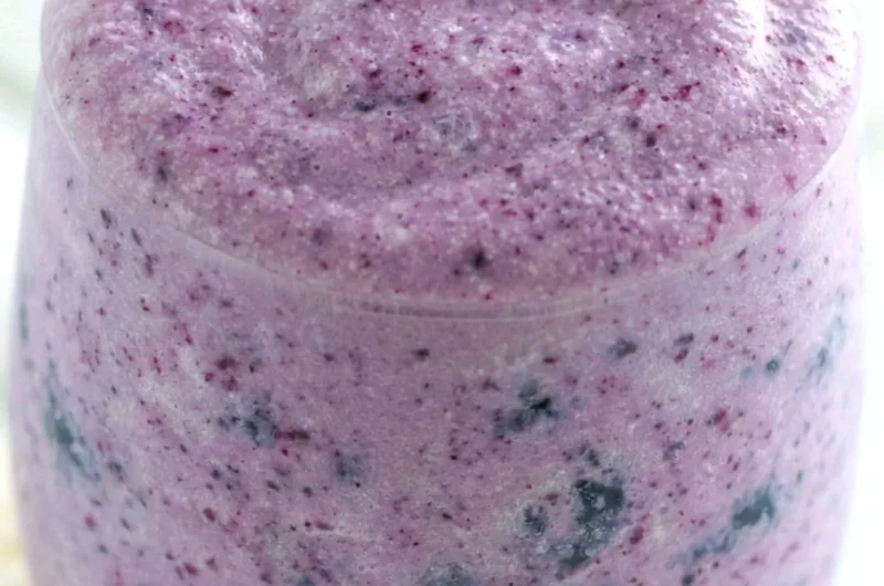 Healthy blueberry banana protein smoothie in a glass with fresh fruits around it