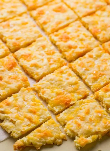 Cozy homemade sourdough crackers topped with cheddar cheese on a plate.