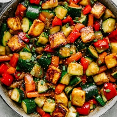 Zucchini stir fry with tofu served in a colorful bowl alongside fresh vegetables.