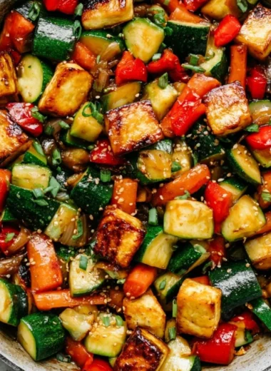 Zucchini stir fry with tofu served in a colorful bowl alongside fresh vegetables.